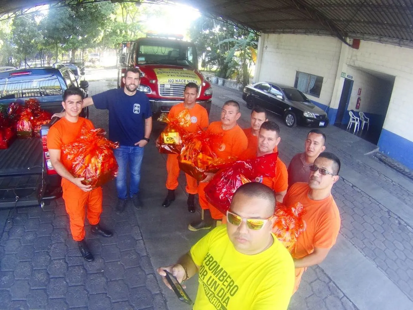 Bomberos con uniforme de trabajo naranja junto a una unidad del Cuerpo de Bomberos